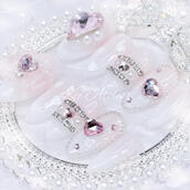 Custom press-on nail set by Kei Atelier featuring pink and white glitter gels, heart and bow charms, and rhinestones